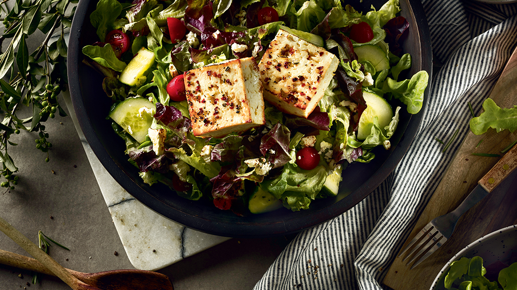 Feta salad in black bowl with two large feta squares on top