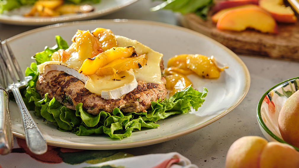 Open face turkey burger on bed of lettuce topped with peach slices and brie cheese.