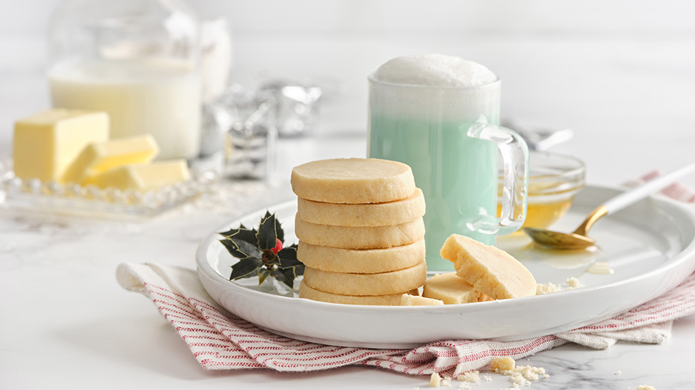 Stack of icebox cookies on an oval, white plate with a clear mug with blue milk beverage.