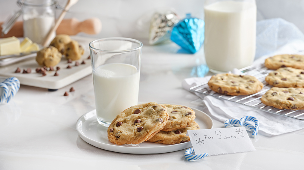 A round white plate with three chocolate chip cookies and a glass of milk.